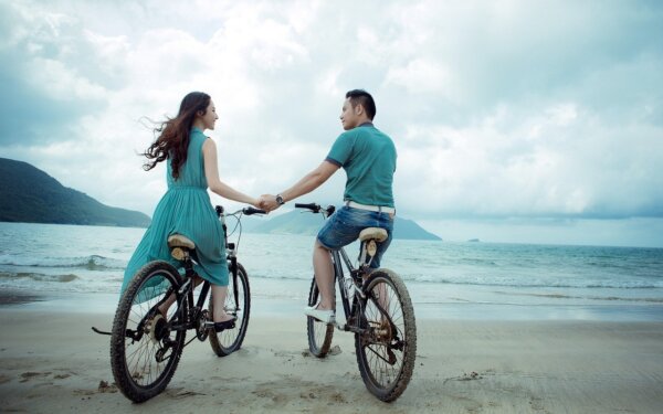 海のある砂浜で自転車に乗る男女2人